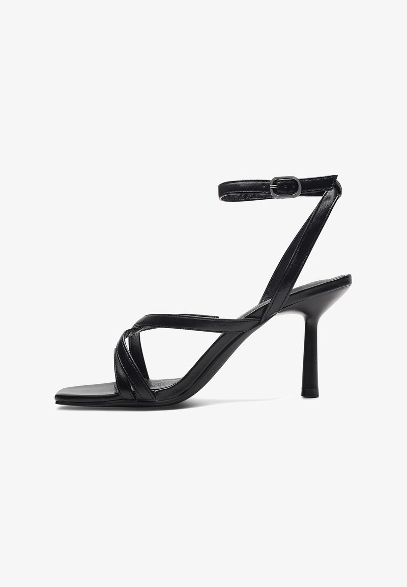 Mustat korkokengät, joissa on ristikkäiset hihnat, neliömäinen kärki ja nilkkahihna soljella. Valmistettu sileästä nahasta matalla pinnalla.