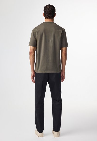 Kaki bomulds-T-shirt med korte ærmer, rund halsudskæring og lige snit, parret med sorte bukser og beige sneakers. Minimalistisk design.