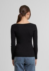 Pulover negru, cu model striat, mâneci lungi și decolteu larg. Croiala mulată evidențiază talia. Textură netedă, stil minimalista.