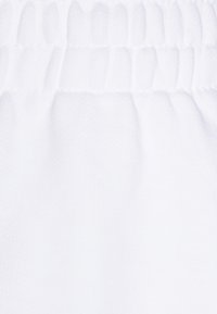 Biała tkanina o gładkiej strukturze, z marszczonym elastycznym pasem. Powierzchnia jest jednolita, bez widocznych wzorów czy akcentów.