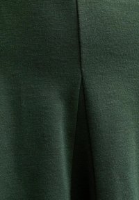 Ciemnozielona tkanina z widoczną drobną fakturą dzianiny i centralnym nachodzącym na siebie szwem tworzącym delikatny cień.