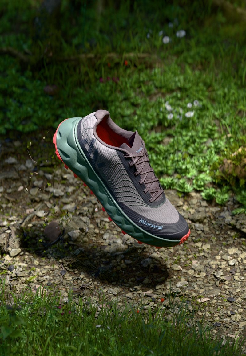 Chaussure de sport grise avec une tige texturée, une semelle intermédiaire verte et une semelle extérieure rouge. Présente des lacets et un logo sur le côté, conçue pour une utilisation en extérieur.