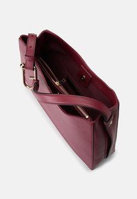 Borsa a tracolla in pelle bordeaux con finitura texturizzata, dotata di una tasca interna con zip e una lunga tracolla. Dettagli in hardware dorato.