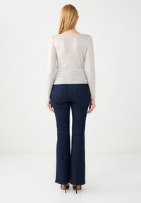 Jasnoszara bluzka z długim rękawem o dopasowanej talii, zestawiona z granatowymi dżinsami dzwonami. Materiał jest gładki, o delikatnym połysku.