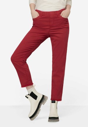 Pantaloni di cotone rossi con vita elasticizzata, dotati di due tasche laterali e orli sfrangiati. Abbinati a stivaletti bianchi alla caviglia con accenti neri.