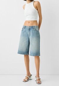 Ljust tvättade denim Bermuda-shorts med avslappnad passform, med femficksdesign och upplottade fållar. Matchas med en ärmlös vit crop top.