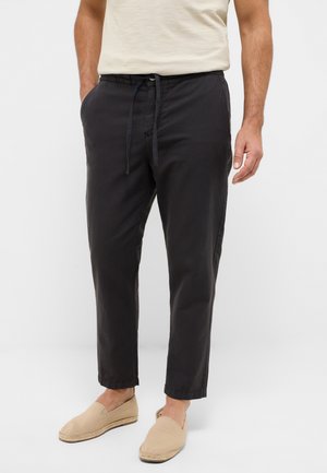 Dunkelgraue, leichte Hose mit einem Kordelzugbund, seitlichen Taschen und schmal zulaufenden Beinen, kombiniert mit beigen Espadrilles.