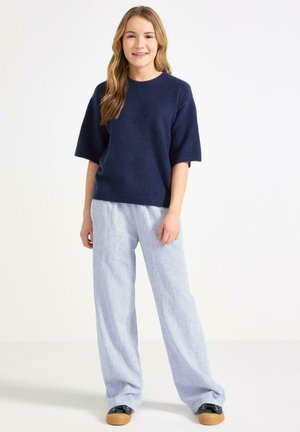 Marineblauw, korte mouwen gebreid bovenstuk gecombineerd met lichtblauw en wit gestreepte, wijde broek. Zwarte schoenen met een plateauzool.