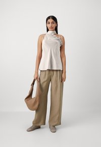 Top senza maniche grigio chiaro con dettagli a balze, abbinato a pantaloni larghi in lino beige e una morbida borsa marrone. Scarpe grigie a fantasia completano il look.