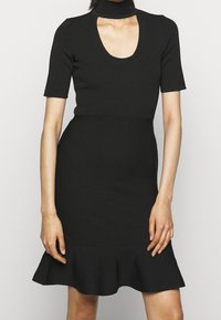 Robe noire côtelée avec manches courtes, encolure dégagée et ourlet évasé. Le tissu a une finition texturée, et la silhouette est ajustée à la taille.