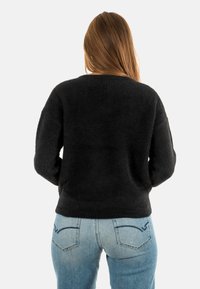 Pull noir texturé avec une coupe décontractée et des épaules tombantes, associé à un jean bleu clair avec deux poches arrière et des détails de couture.