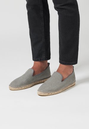 Zapatos de lona grises sin cordones con un upper texturizado, que cuentan con una suela de yute beige, punta redonda y sin cierres visibles.