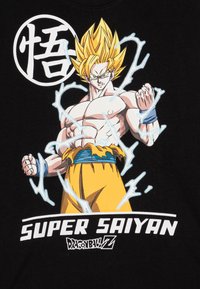 Fekete póló, amelyen egy izmos, szőke hajú karakter látható, kék akcentussal, világoskék energiafutamokkal körülvéve. A felirat: "SZUPER SAIYAN."