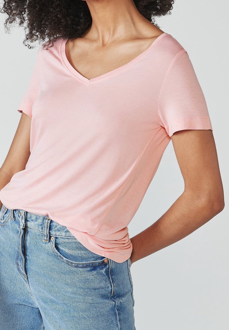 Femme portant un T-shirt rose clair à col en V rentré dans un jean denim bleu taille haute, la main posée sur la hanche.