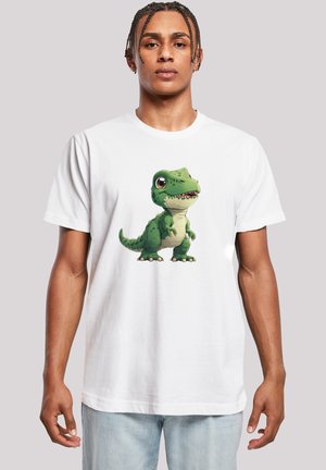 White crewneck t-shirt featuring a cartoon green dinosaur graphic, with detailed scales and a smiling expression, in front of a plain gray background.