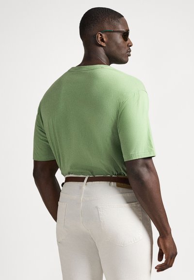 Πράσινο κοντομάνικο μπλουζάκι με άνετη εφαρμογή, συνδυασμένο με ανοιχτό μπεζ παντελόνι και καφέ ζώνη. Το ύφασμα φαίνεται υφασμάτινο.