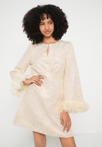 Rochie de culoare crem cu finisaj texturat, având un decolteu tip cheie și mâneci clopot decorate cu accente pufoase, stratificate, la manșete.