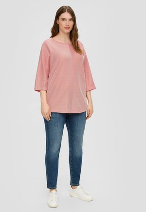 Rood-wit gestreepte top met een losse pasvorm, ronde halslijn en mouwen tot de elleboog, gecombineerd met blauwe jeans en witte sneakers.