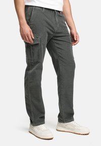 Grå kordfløjspants med rette ben, som har en sidelomme og teksturert stoff, kombinert med hvite sneakers.