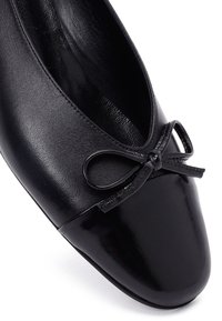 Ballet flat in pelle nera con punta lucida e un piccolo fiocco sulla tomaia, dotato di una fodera interna liscia.