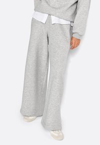 Pantaloni della tuta grigi a gamba larga realizzati in tessuto morbido, con un design affusolato, vita elastica e abbinati a una camicia bianca con colletto sotto.