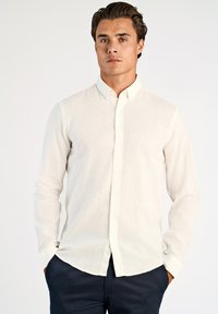 Camicia bianca a maniche lunghe con bottoni in tessuto di lino leggero con una texture sottile; presenta un colletto classico e un orlo dritto.