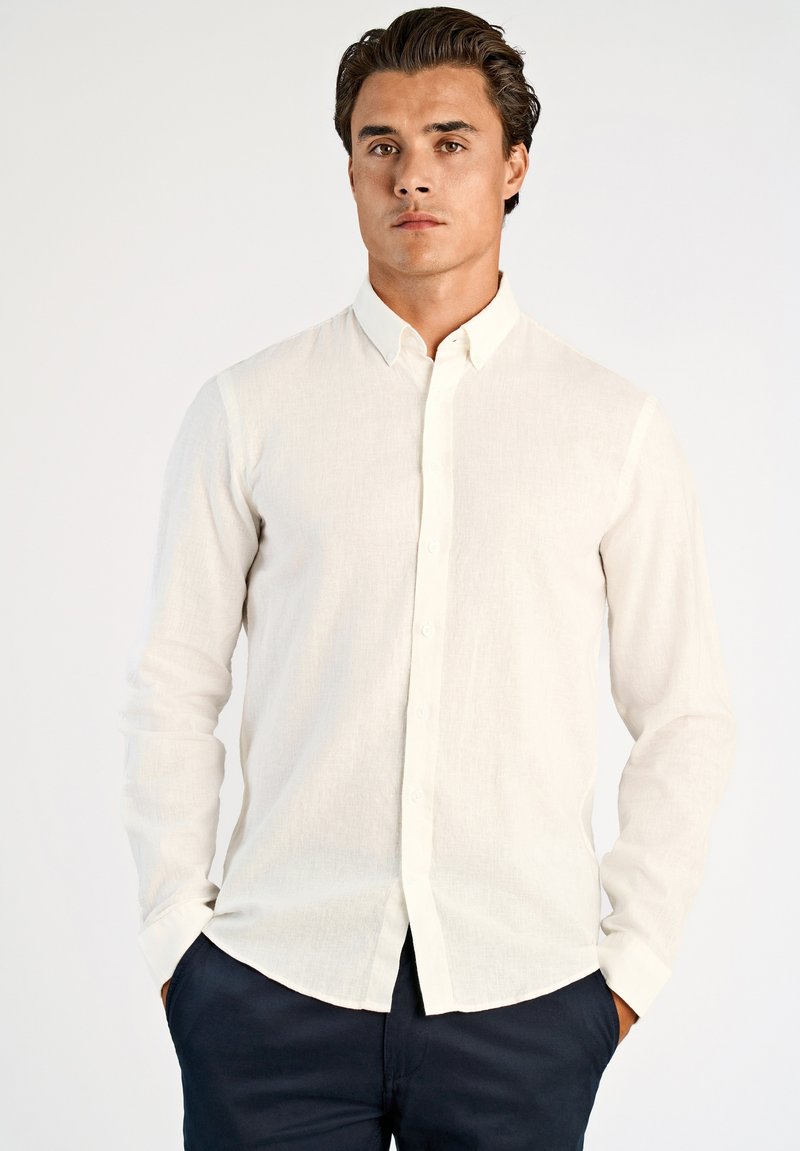 Camicia bianca a maniche lunghe con bottoni in tessuto di lino leggero con una texture sottile; presenta un colletto classico e un orlo dritto.