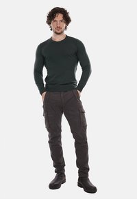Jersey de punto verde con un cuello redondo, combinado con pantalones cargo oscuros que tienen múltiples bolsillos, y botas de tobillo negras.