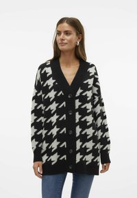 Svart och vit houndstooth-mönstrad cardigan med V-ringning, oversize passform och fem svarta knappar fram. Stickad tyg.