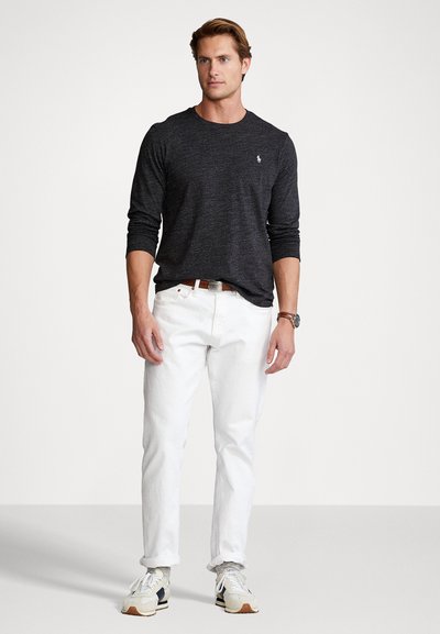 Heren langemouw, donkergrijze shirt met een ronde hals, gecombineerd met witte jeans met opgerolde mouwen en multicolore sneakers.