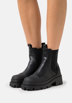Bottines noires avec un design en cuir serpent texturé, semelles en caoutchouc, panneaux latéraux élastiques et tirettes pour un enfilage facile.