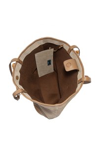 Borsa a forma di secchiello in suede beige con dettagli in pelle marrone. L'interno presenta una fodera brown testurizzata e una piccola tasca con etichetta.