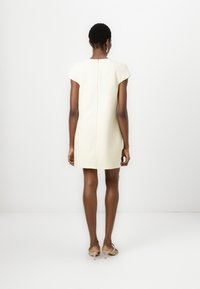 Short sleeve, cream dress with a fitted silhouette, textured fabric, and a zip closure at the back. Knee-length with a straight cut.