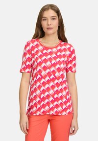 Kortærmet t-shirt med et geometrisk mønster i pink og hvid, rund halsudskæring og blødt, strækbart stof. Bæres sammen med koralfarvede bukser.