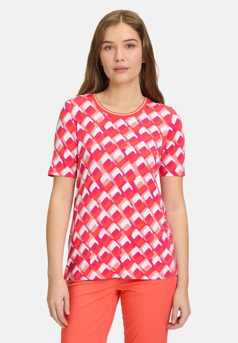 Kortærmet t-shirt med et geometrisk mønster i pink og hvid, rund halsudskæring og blødt, strækbart stof. Bæres sammen med koralfarvede bukser.