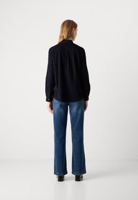 Chemise à manches longues bleu marine avec un col à boutons, coupe décontractée et détail de empiècement au dos, assortie à un jean flare bleu clair et des bottines noires.