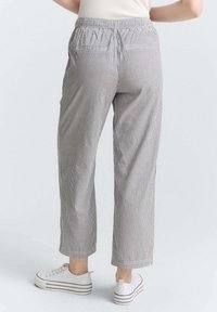 Pantalons en tissu léger à rayures, avec une taille élastique, longueur cropped, deux poches arrière, et assortis à des baskets blanches.
