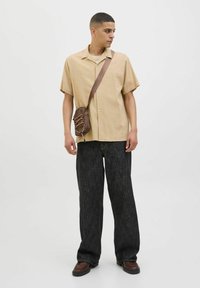 Camisa corta de manga corta marrón, de tela texturizada, beige claro, abotonada; vaqueros oscuros de pierna ancha, de mezclilla, con un ligero brillo; bolso cruzado marrón, con detalle de cuerda.