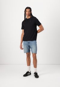 T-shirt preta de gola redonda, calções de ganga azul claro, sapatilhas pretas com detalhes brancos e meias brancas de cano curto. Tecido suave, corte descontraído.