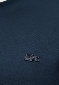 Tissu bleu foncé avec un petit logo de crocodile brodé sur la zone de la poitrine d'un vêtement.