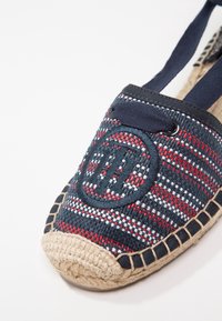 Chaussure espadrille en tissu tissé bleu marine, rouge et blanc, bout rond, semelle en jute tressée et lacets bleus marins passés dans des œillets en métal.