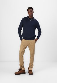 Navy zip-neck sweater, khaki pants, and brown boots with faux fur cuffs. The outfit features a casual design and contrasting colors.