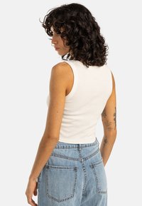 Débardeur blanc côtelé avec une coupe ajustée. Associe à un jean taille haute bleu clair arborant un style classique à cinq poches et une couture visible.