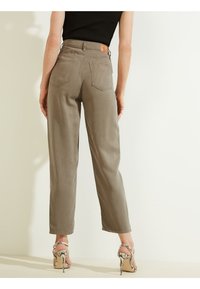 Pantalones grises claros con cintura alta y corte recto, que presentan dos bolsillos traseros y un parche de cuero marrón, combinados con sandalias de tacón alto con tiras.
