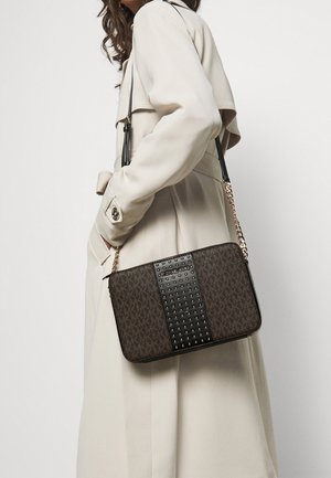 Borsa a tracolla marrone con motivo, pannello nera con borchie, tracolla in catena e texture morbida, appoggiata su un trench coat beige.