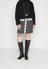 Černá zkrácená bunda s velkými kapsami, v kombinaci s černobílou kostkovanou sukní s knoflíkovými detaily. Černé vysoké boty po kolena.