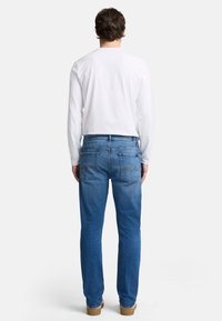 Blå denimjeans med rak passform, utrustad med två bakfickor med stickade detaljer, kombinerat med en vit skjorta med långa ärmar.