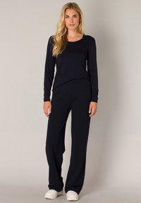 Marineblauwe top met lange mouwen en broek met wijde pijpen, gemaakt van een soepele stof. De top heeft een ronde halslijn; de broek heeft een elastieken tailleband. Witte sneakers.