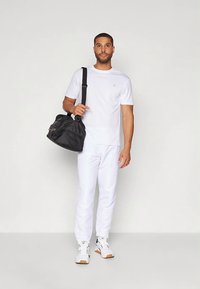 Biała koszulka z krótkim rękawem i białe spodnie dresowe, zestawione z czarną torbą sportową i białymi trampkami. Prosty, czysty design z minimalnymi akcentami.