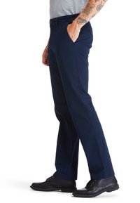 Mörkblå byxor med rak passform, med knappstängning, sidofickor och mjuk bomullstyg. Bärs med svarta skor.